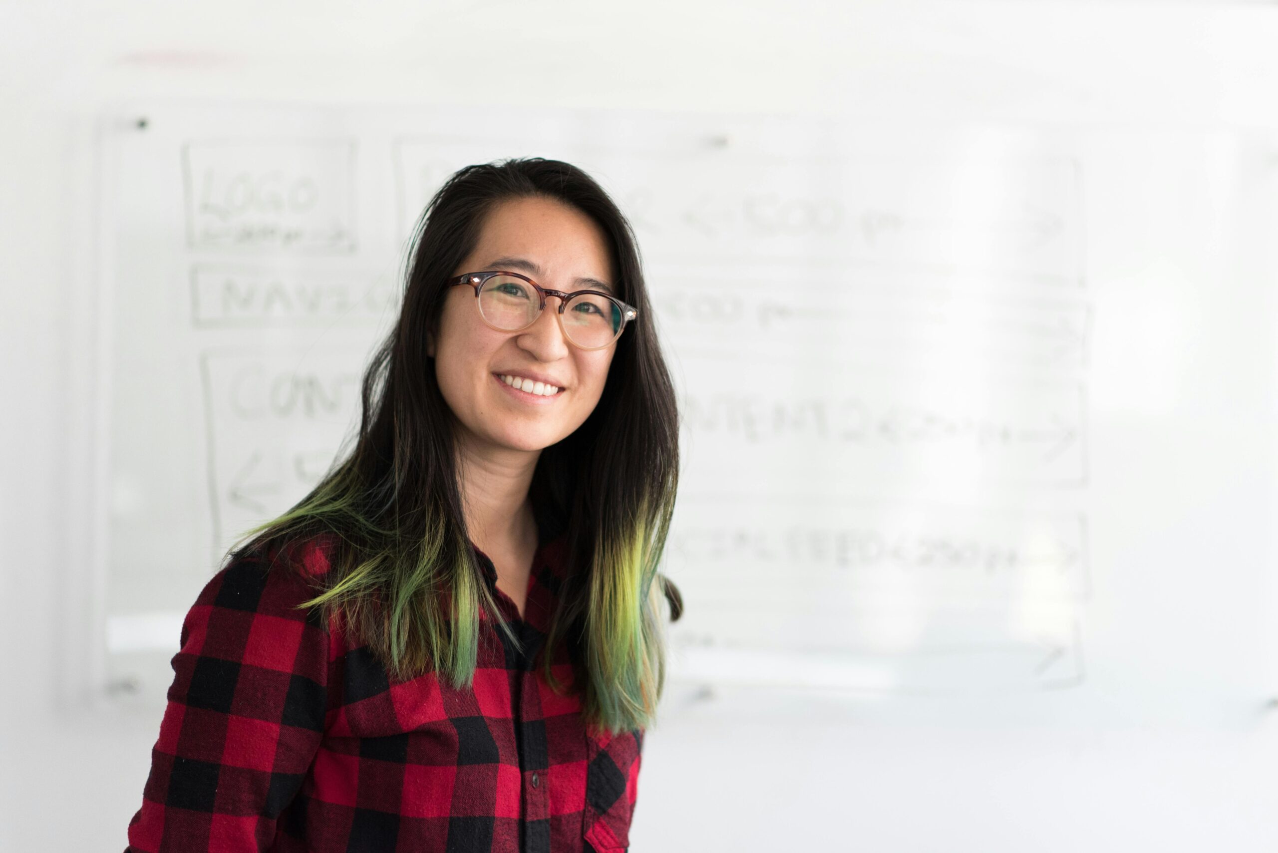 Confident young woman smiling in front of a whiteboard indoors.